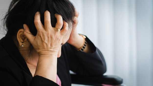 Senior Aziatische vrouw van middelbare leeftijd die pijn voelt en lijdt aan plotselinge hoofdpijn en herseninfarcten en haar hoofd vasthoudt met een gestrest gezicht. Concept van hersen- en hoofdprobleem.