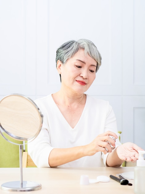 Senior Azië-vrouw spuit thuis parfum.