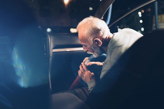 Senior beard man cleaning his car with vacuum cleaner in the evening at car wash station