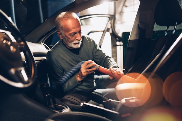 Senior beard man cleaning his car with vacuum cleaner in the evening at car wash station