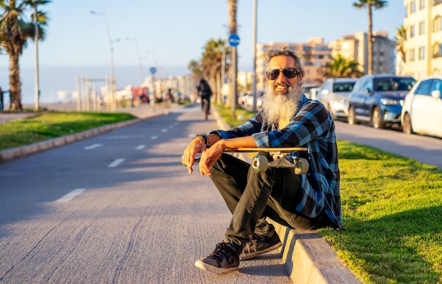 Senior beard man with skateboard sitting on the street smiling happy