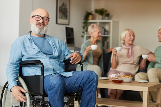 Senior bearded disabled sitting in wheelchair and smiling at camera at nursing home