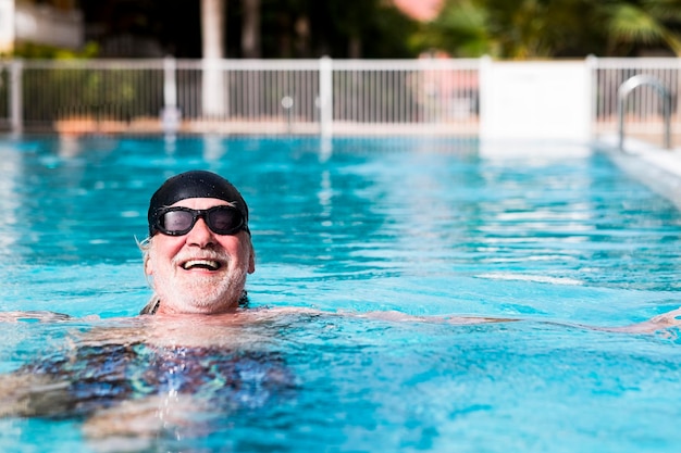 야외 수영장에서 즐거운 수염을 기른 노인은 검은색 수영 모자와 고글을 쓰고 활동적인 은퇴한 노인들을 일기 활동으로 건강한 활동을 즐깁니다.
