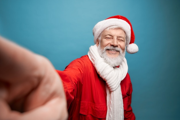 Senior bearded man in Santa costume and scarf taking selfie