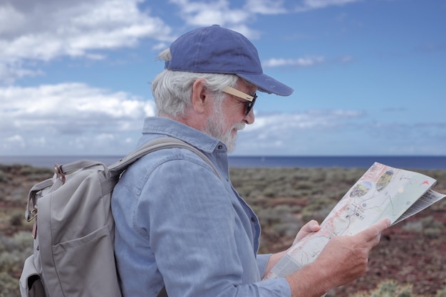 Senior bearded man with backpack walking in countryside looking at footpaths map