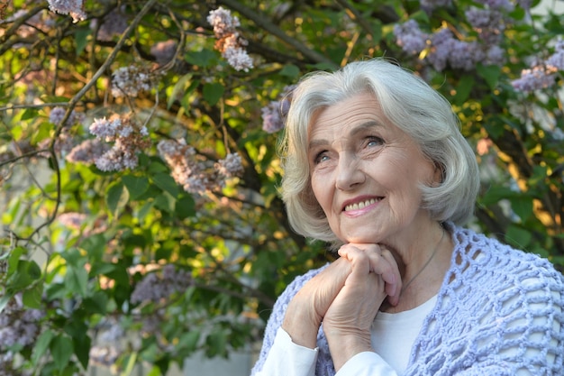 Photo senior beautiful happy woman posing by lilacs in park