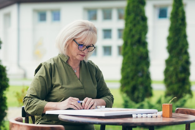 Senior beautiful woman sitting on a chair and paints a picture