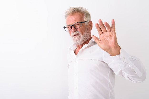 senior bebaarde man kijkt walgend terwijl stophandteken wordt weergegeven en het dragen van een bril op wit