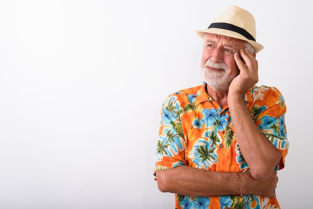 senior bebaarde toeristische man denken terwijl op zoek gestrest en hoed dragen op wit