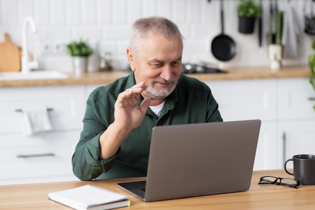 Senior blanke man die laptop gebruikt voor videogesprekken om thuis te zitten