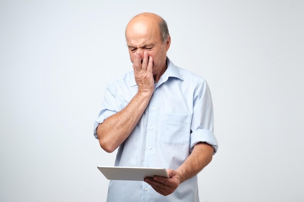 Senior blanke man walgt van wat hij ziet op een tablet