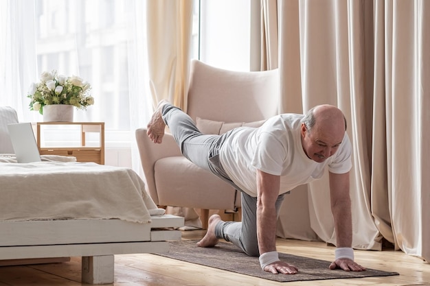 Senior blanke mannen beoefenen yoga asana chakravakasana vogel pose thuis