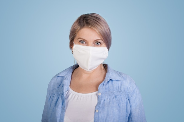 Senior blanke vrouw in wit t-shirt en shirt poseren op een blauwe muur met een medisch masker op het gezicht