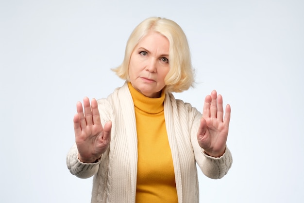 Senior blonde woman wearing yellow and white clothes showing stop sign