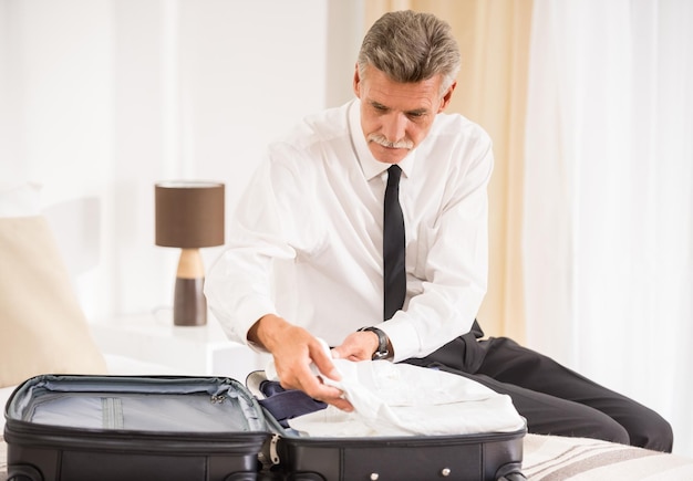 Foto senior uomo d'affari che imballa i vestiti in valigia nella camera d'albergo