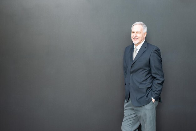 Senior business man standing next to a black wall