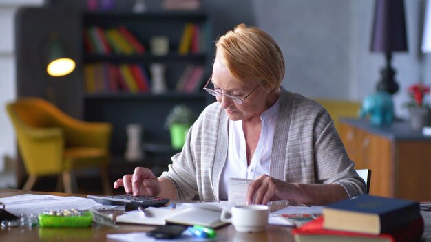 Фото Старшая деловая женщина держит бумажный счет с помощью калькулятора