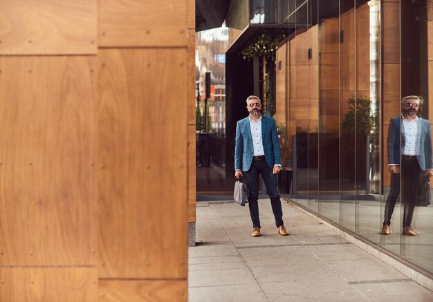 A senior businessman in a blue suit with a briefcase walking through the city.