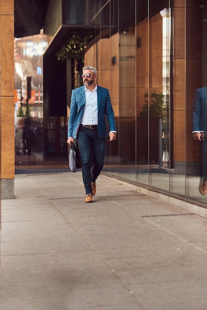 A senior businessman in a blue suit with a briefcase walking through the city.