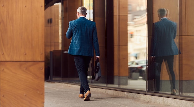 A senior businessman in a blue suit with a briefcase walking through the city.