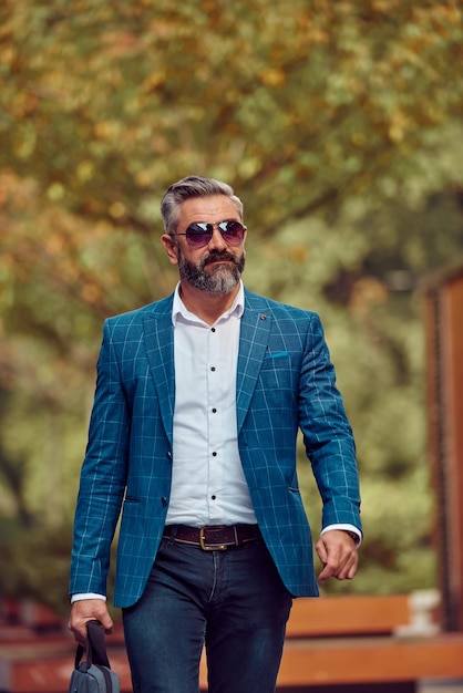 A senior businessman in a blue suit with a briefcase walking through the city.