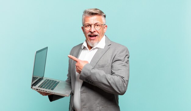 Senior businessman looking excited and surprised pointing to the side and upwards to copy space