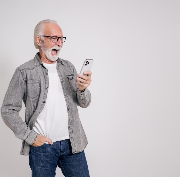 Senior businessman reading message over mobile phone and screaming ecstatically on white background