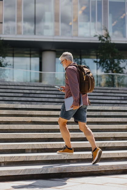 Photo a senior businessman in a shirt and shorts climbs the steps to the office with a laptop