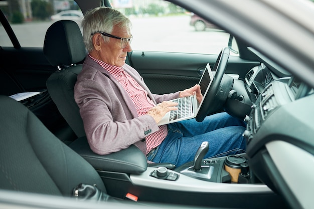 車でラップトップを使用して上級ビジネスマン