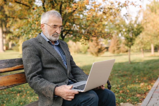 Senior businessman using laptop outside Elderly man in gray jacket use laptop in the park