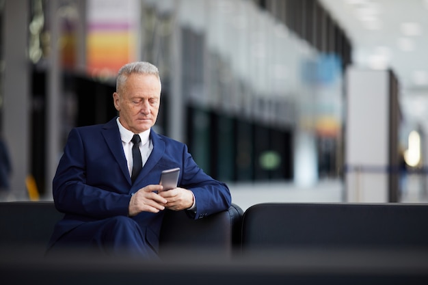 Senior Businessman Using Smartphone in Lobby