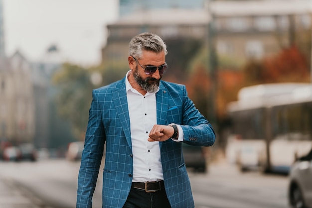 Senior businessman walking in the city, carrying a bag and using a watch.