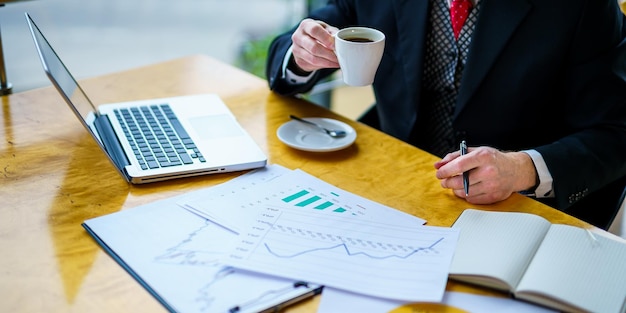 L'uomo d'affari senior indossa una camicia bianca e un abito scuro bere caffè a tavola con documenti su di esso concetto di business