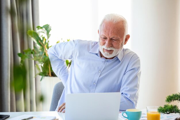 Photo senior businessman working sitting at desk suffers from lower back pain damage of intervertebral discs spinal joints compression of nerve roots caused by wrong posture and sedentary work