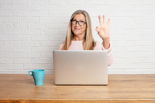 Senior businesswoman smiling and looking satisfied and happy, counting number three with fingers.