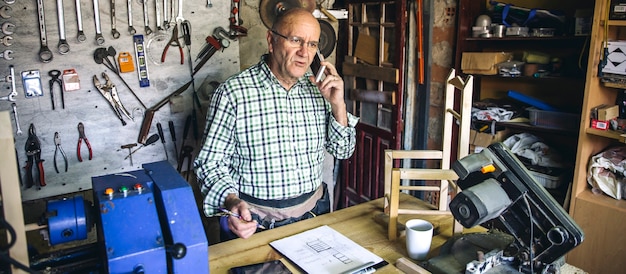 Photo senior carpenter talking on the phone in his workshop