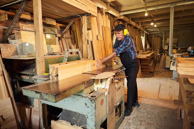 Старший плотник в униформе работает на деревообрабатывающем станке на столярном производстве