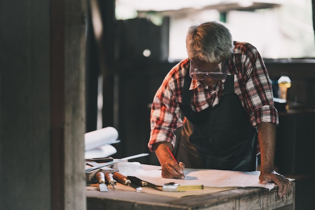 Foto falegname senior che usa la matita e cerca il progetto per lavorare su macchine per la lavorazione del legno nella falegnameria l'uomo lavora in una falegnameria