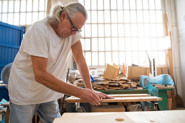 Senior carpenter working on wood craft at workshop producing wooden furniture