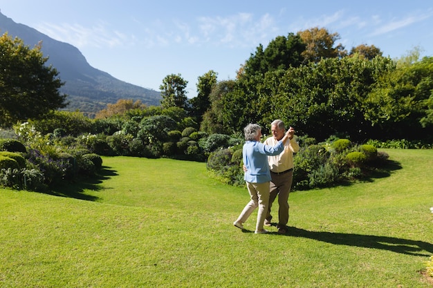 Senior caucasian couple dancing together in sunny garden. retreat, retirement and happy senior lifestyle concept.