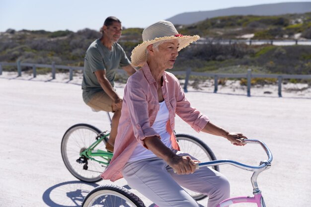 Senior Caucasian couple enjoying time at the beach on a sunny day, riding bikes with sand in the background