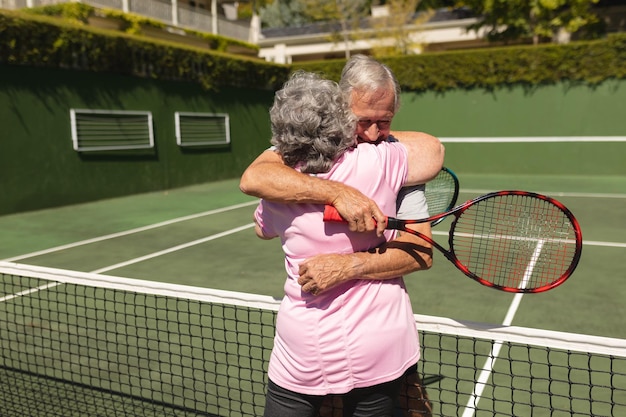 Foto una coppia caucasica anziana che gioca a tennis insieme sul campo abbracciandosi