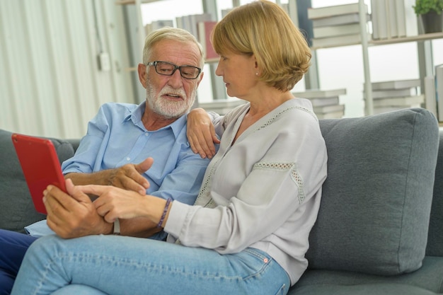 Senior caucasian couple using tablet sitting on sofa