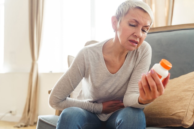 Senior Caucasian female with her hand on the stomach looking at a bottle of pills