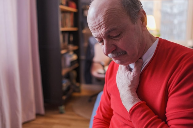 Senior caucasian man having sore throat and touching his neck at home