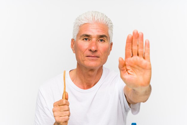 Senior caucasian man holding a teethbrush isolated standing with outstretched hand showing stop sign, preventing you.