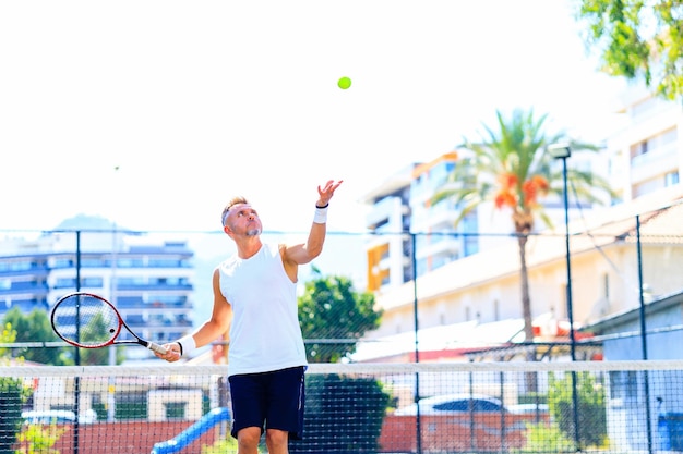 Foto uomo caucasico anziano che gioca a tennis sul campo tenendo la luce del giorno della racchetta da tennis all'aperto all'aria aperta