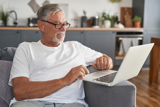 Senior caucasian man sitting at couch and using laptop