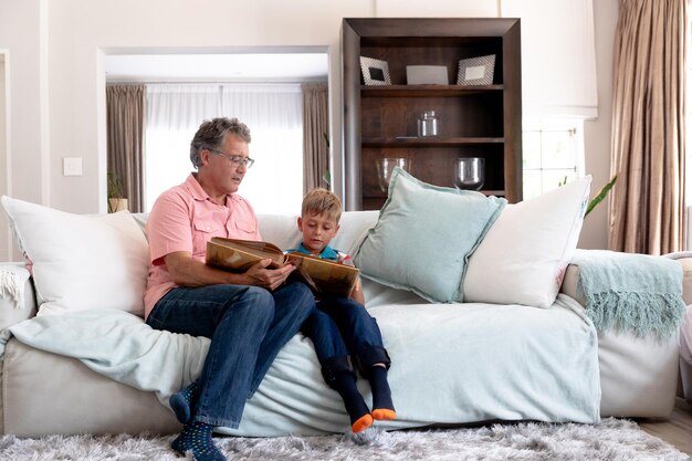 Photo senior caucasian man spending time at home with his grandson, sitting on a couch and watching a family album.