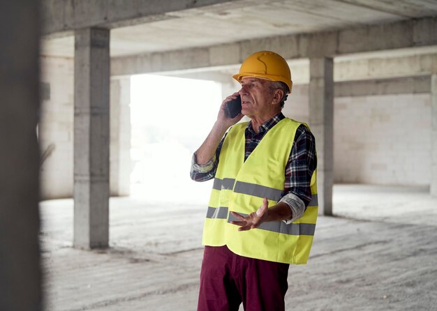 Photo senior caucasian man talking by mobile phone on the construction site